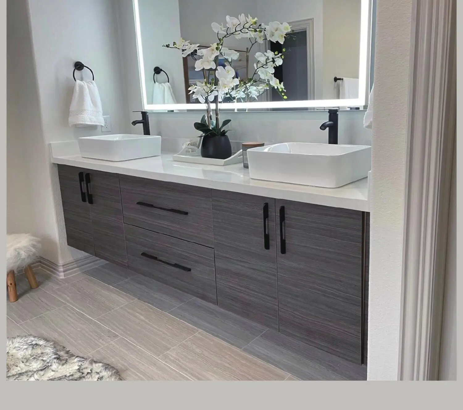Floating double vanity in grey woodgrain with vessel sinks and a backlit mirror